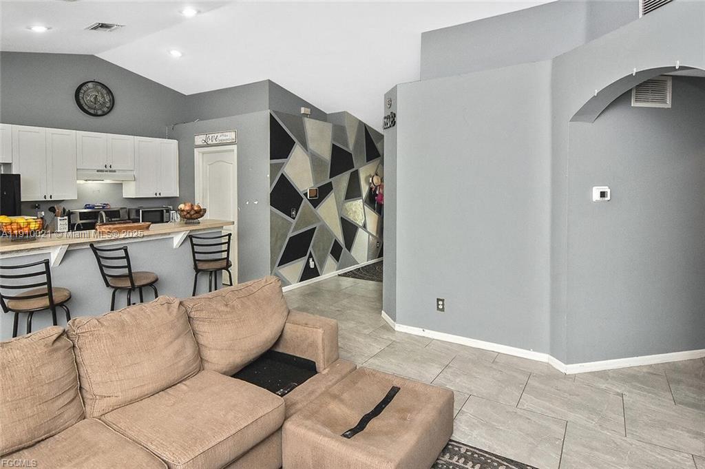 A living room features a tan sofa, a breakfast bar, and a geometric accent wall — 2612 66 st w, Lehigh Acres FL 33971, LEHIGH ACRES, FL