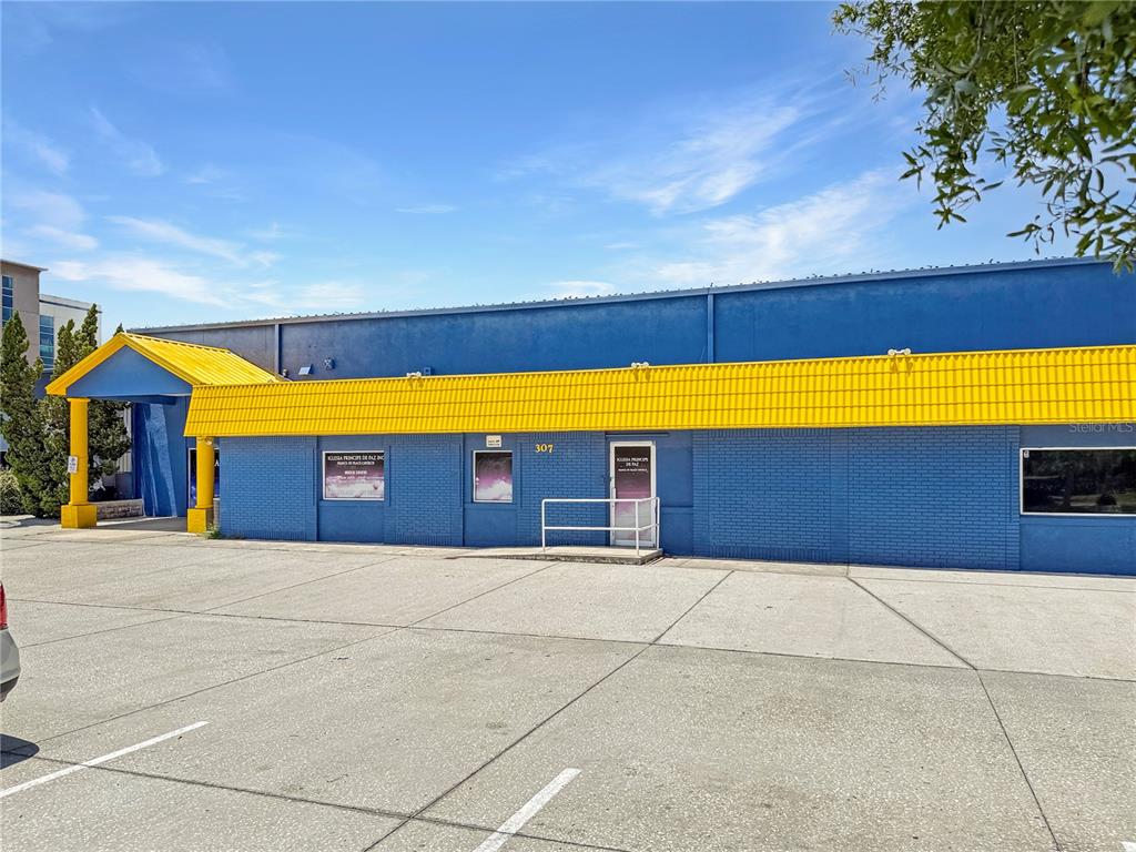 A blue brick commercial building features a yellow metal roof and a paved parking lot — 307 W BASS STREET, KISSIMMEE, FL