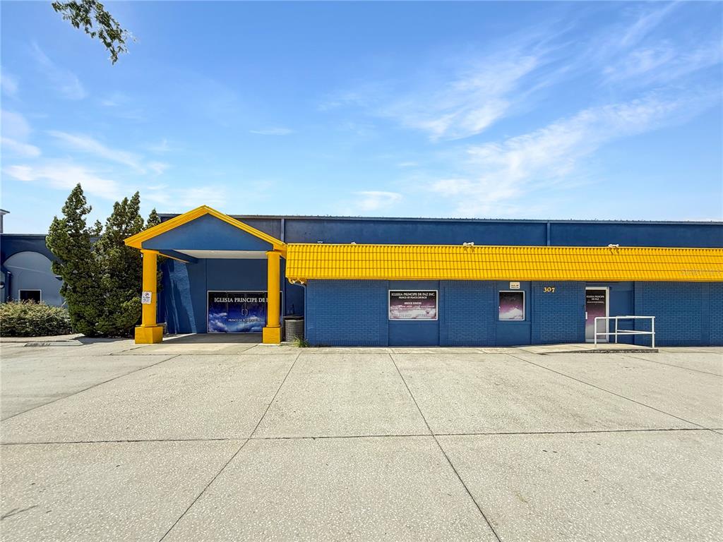A blue commercial building features a yellow roof, a covered entrance, and a concrete parking lot — 307 W BASS STREET, KISSIMMEE, FL