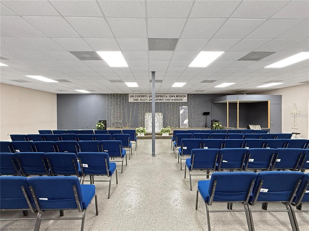 A church sanctuary features rows of blue chairs facing a stage with a central pillar — 307 W BASS STREET, KISSIMMEE, FL