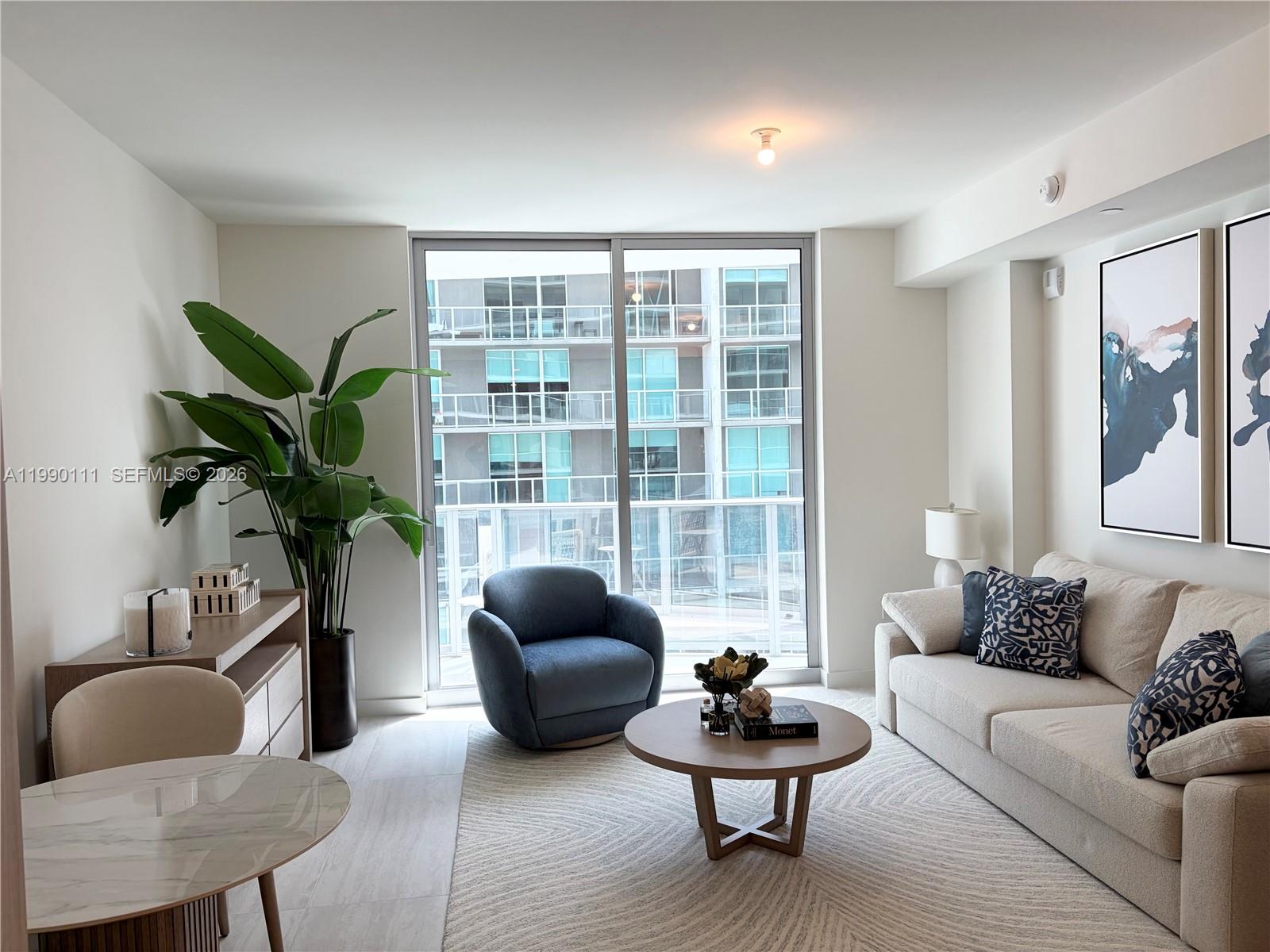 A modern living room features a beige sofa, blue armchair, round coffee table, and balcony — 77 SE 5th street # 2709, Miami FL 33131, MIAMI, FL