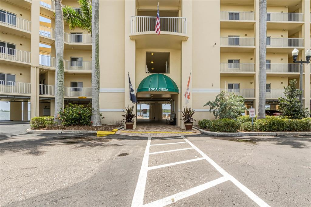The exterior entrance of a multi-story apartment building features a green awning and palm trees — 8800 BAY PINES BOULEVARD UNIT 212, ST PETERSBURG, FL