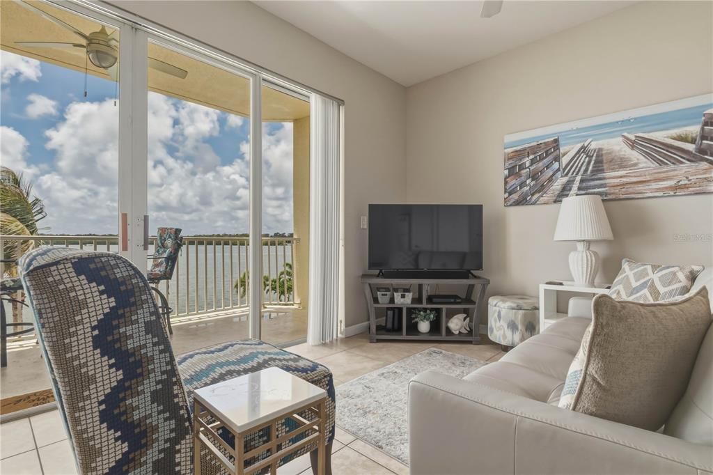 A living room features a sofa, patterned armchair, television, and sliding doors opening to a balcony — 8800 BAY PINES BOULEVARD UNIT 212, ST PETERSBURG, FL