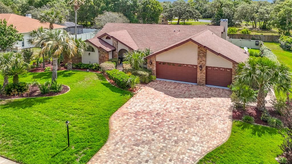 An aerial view shows a single-story house with a brick facade, brown roof, and paver driveway — 4306 RIVER BIRCH DRIVE, SPRING HILL, FL
