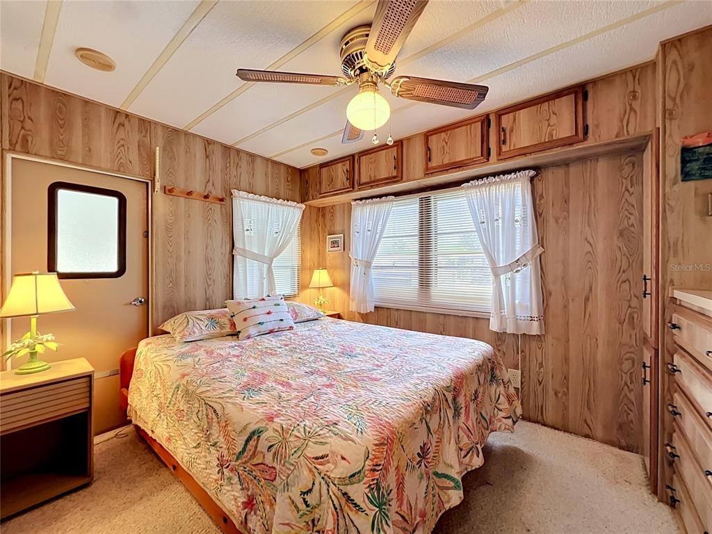 A bedroom features wood-paneled walls, a ceiling fan, a floral bedspread, and built-in storage cabinets — 9000 US HIGHWAY 192 UNIT 766, CLERMONT, FL