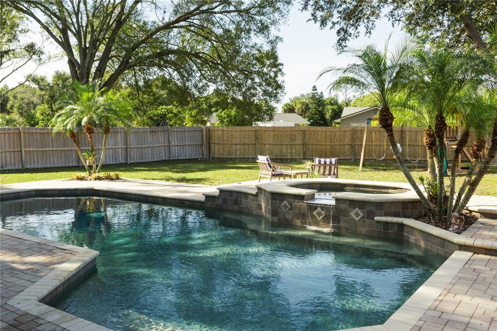 A backyard features a swimming pool with an attached spa, stone decking, and a wooden fence — 8445 SHADY GLEN DRIVE, ORLANDO, FL