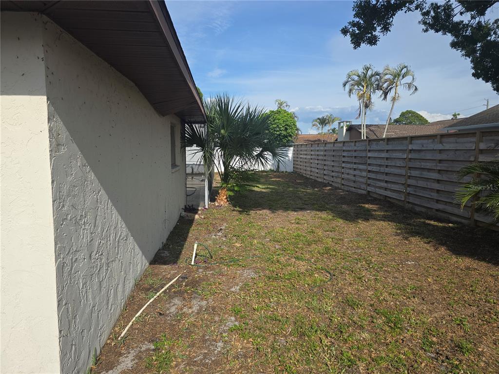 A side yard with a stucco house wall, a wooden fence, and a palm tree — 5403 2ND AVENUE DR NW, BRADENTON, FL