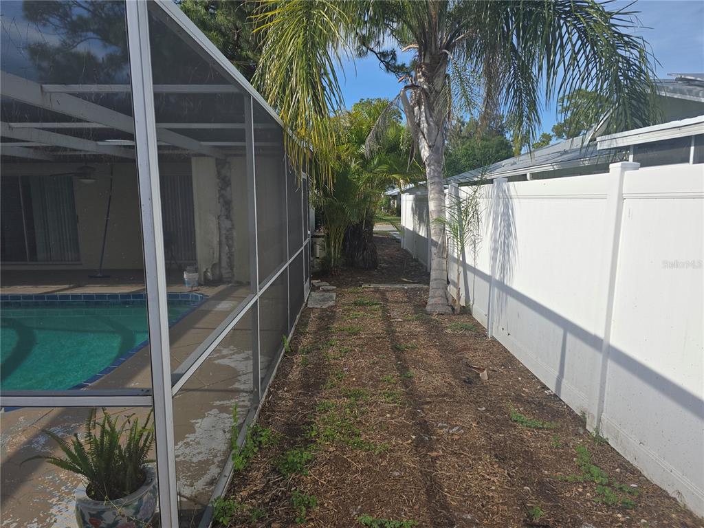 A narrow dirt side yard sits between a screened pool enclosure and a white fence — 5403 2ND AVENUE DR NW, BRADENTON, FL