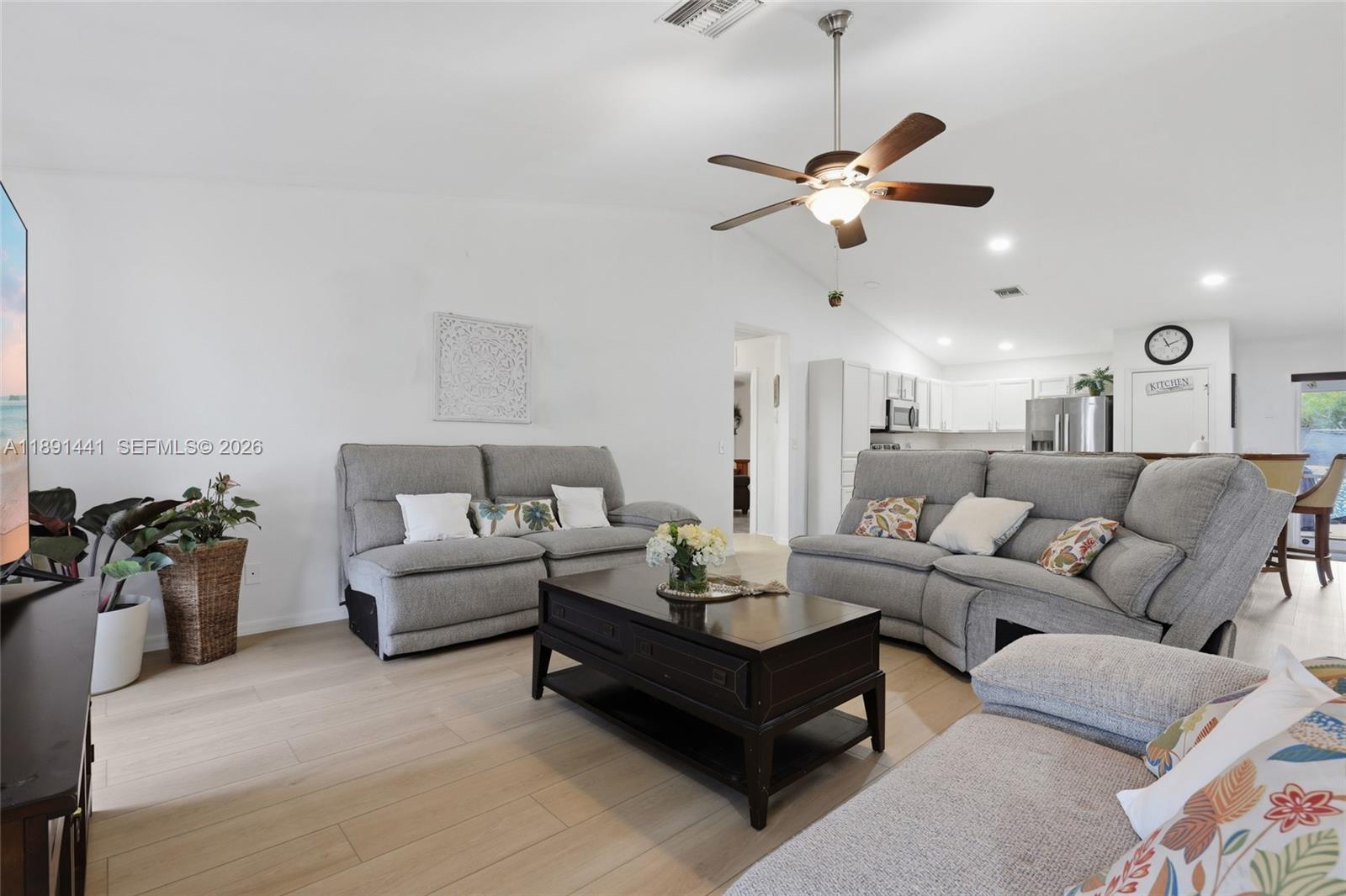 A living room features light wood flooring, gray sectionals, a coffee table, and a ceiling fan — 3003 W 25th St, Lehigh Acres FL 33971, LEHIGH ACRES, FL