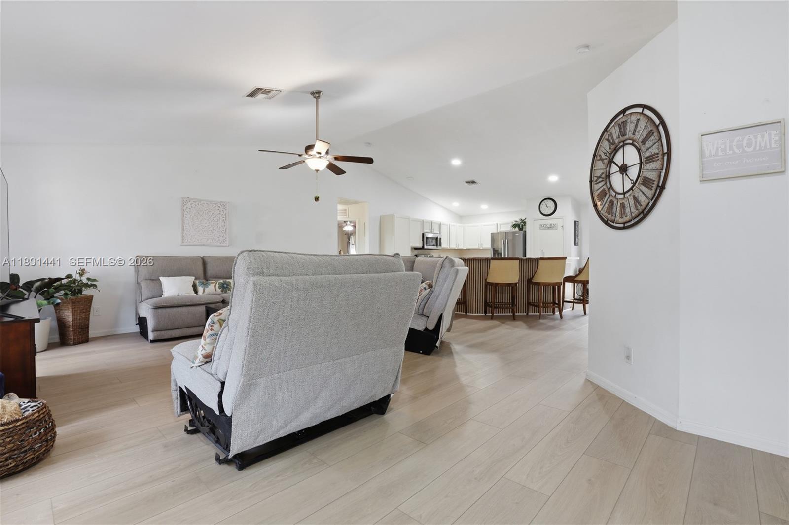 A living room with light wood floors opens into a kitchen with a breakfast bar — 3003 W 25th St, Lehigh Acres FL 33971, LEHIGH ACRES, FL
