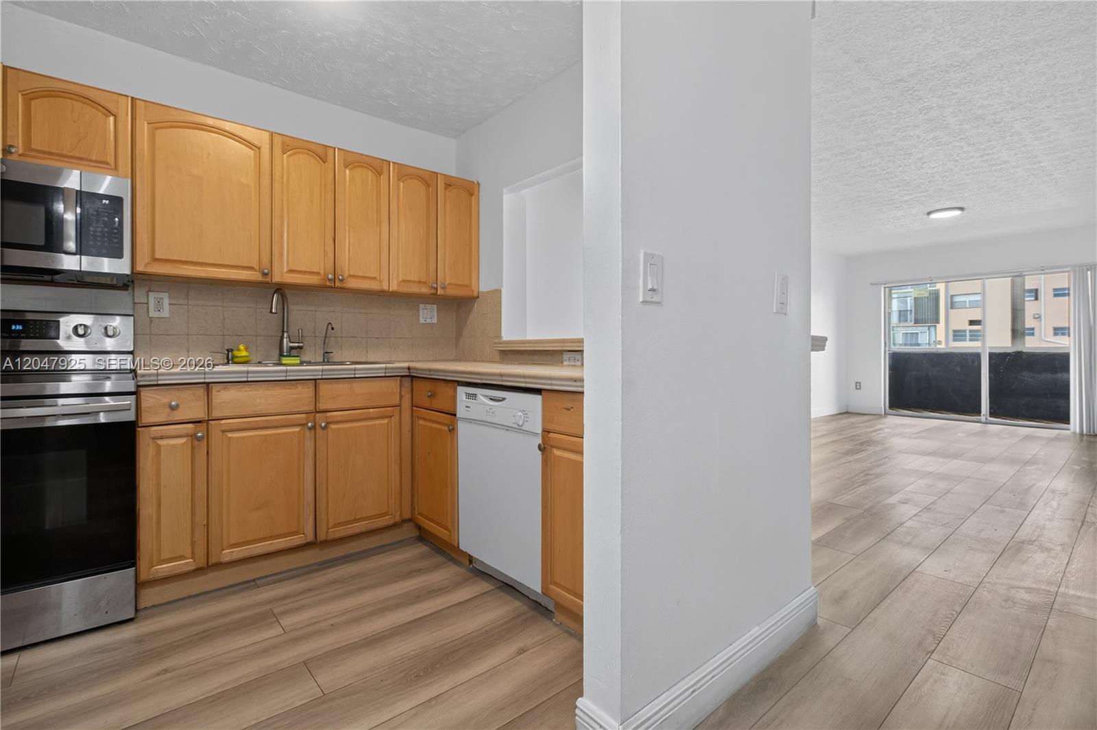 A kitchen with light wood cabinets and a dishwasher opens into a living area — 6070 W 18th Ave # 209, Hialeah FL 33012, HIALEAH, FL