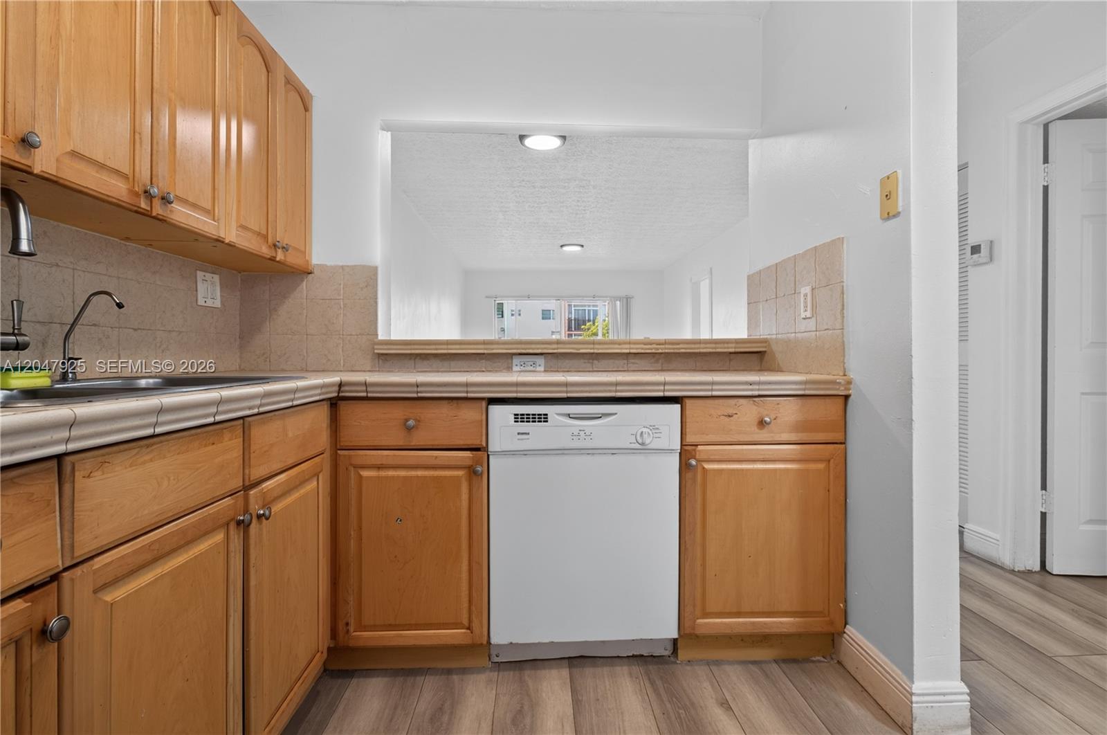 A kitchen features wood cabinets, a white dishwasher, and a tiled countertop with a pass-through — 6070 W 18th Ave # 209, Hialeah FL 33012, HIALEAH, FL