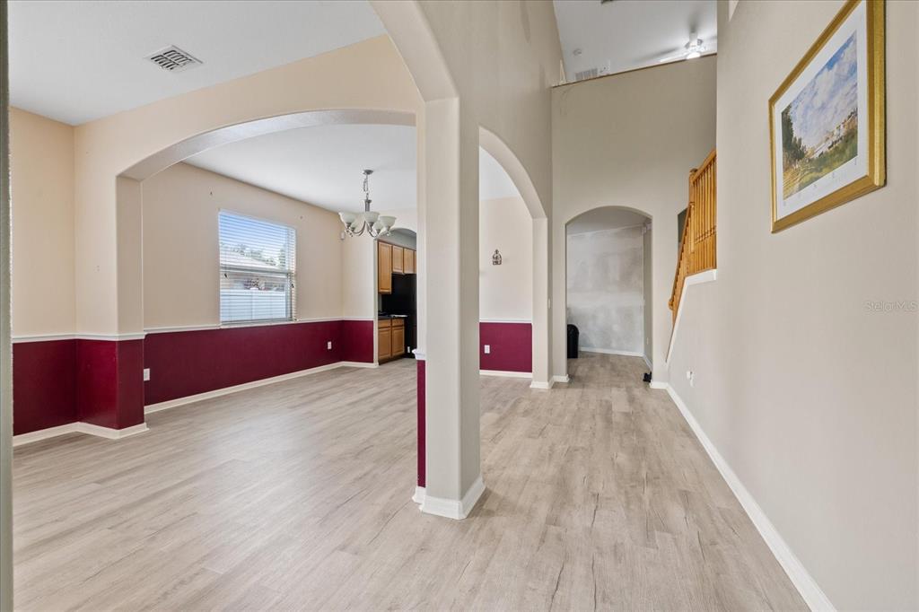 An open-concept living area features arched doorways, light wood-look flooring, and burgundy wainscoting — 2841 TRINITY COTTAGE DRIVE, LAND O LAKES, FL