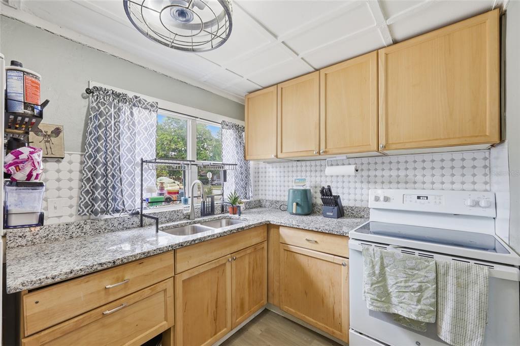 A kitchen features light wood cabinets, granite countertops, a white stove, and a window — 1813 HIGH STREET, LEESBURG, FL