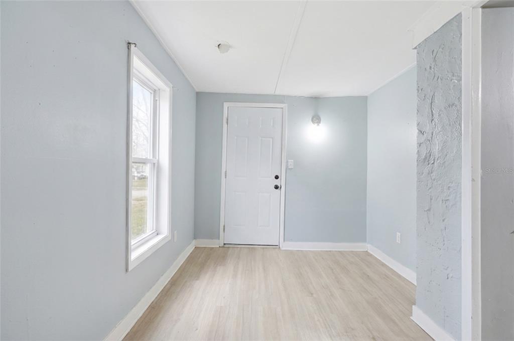 A room with light blue walls, wood-look flooring, a white door, and a single window — 1813 HIGH STREET, LEESBURG, FL