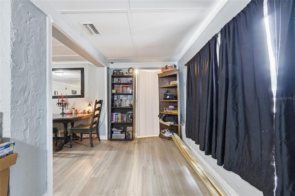 A room with light wood-look flooring, a bookshelf, and a dining area visible through an opening — 1813 HIGH STREET, LEESBURG, FL