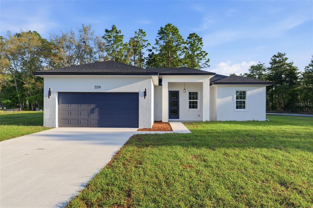 A single-story house with a white stucco exterior, dark roof, and a two-car garage — 559 W HERONSBILL LANE, DUNNELLON, FL