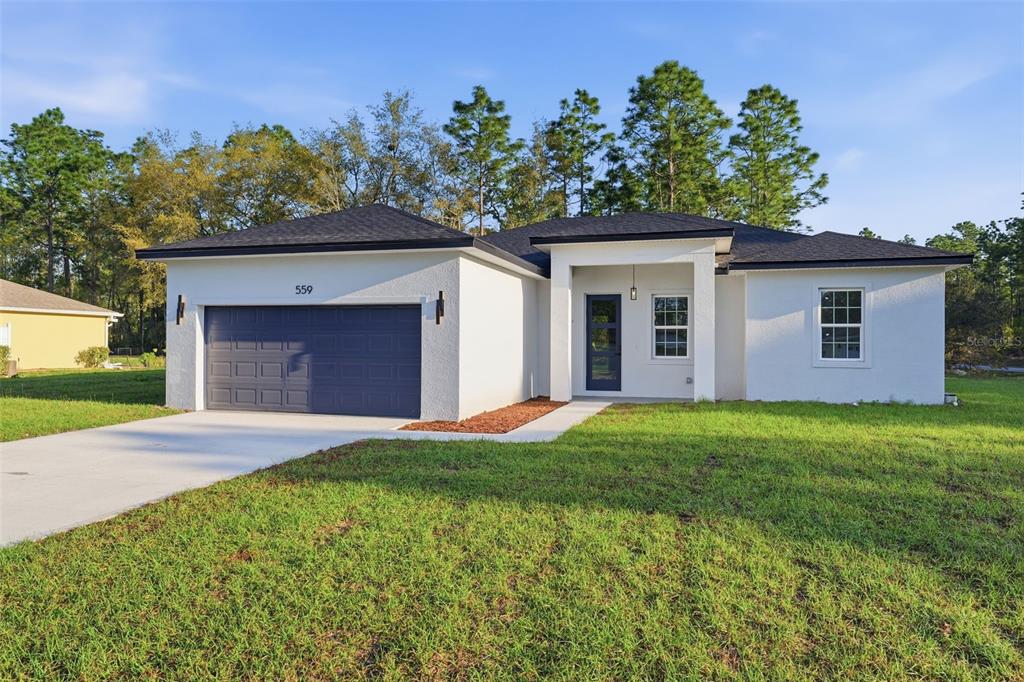 A single-story house with white stucco walls, a dark roof, and a two-car garage — 559 W HERONSBILL LANE, DUNNELLON, FL