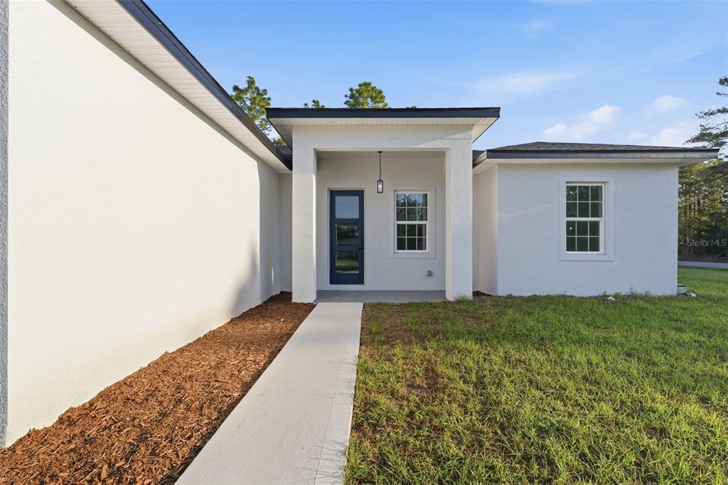 A white stucco house exterior features a dark blue front door and a concrete walkway — 559 W HERONSBILL LANE, DUNNELLON, FL