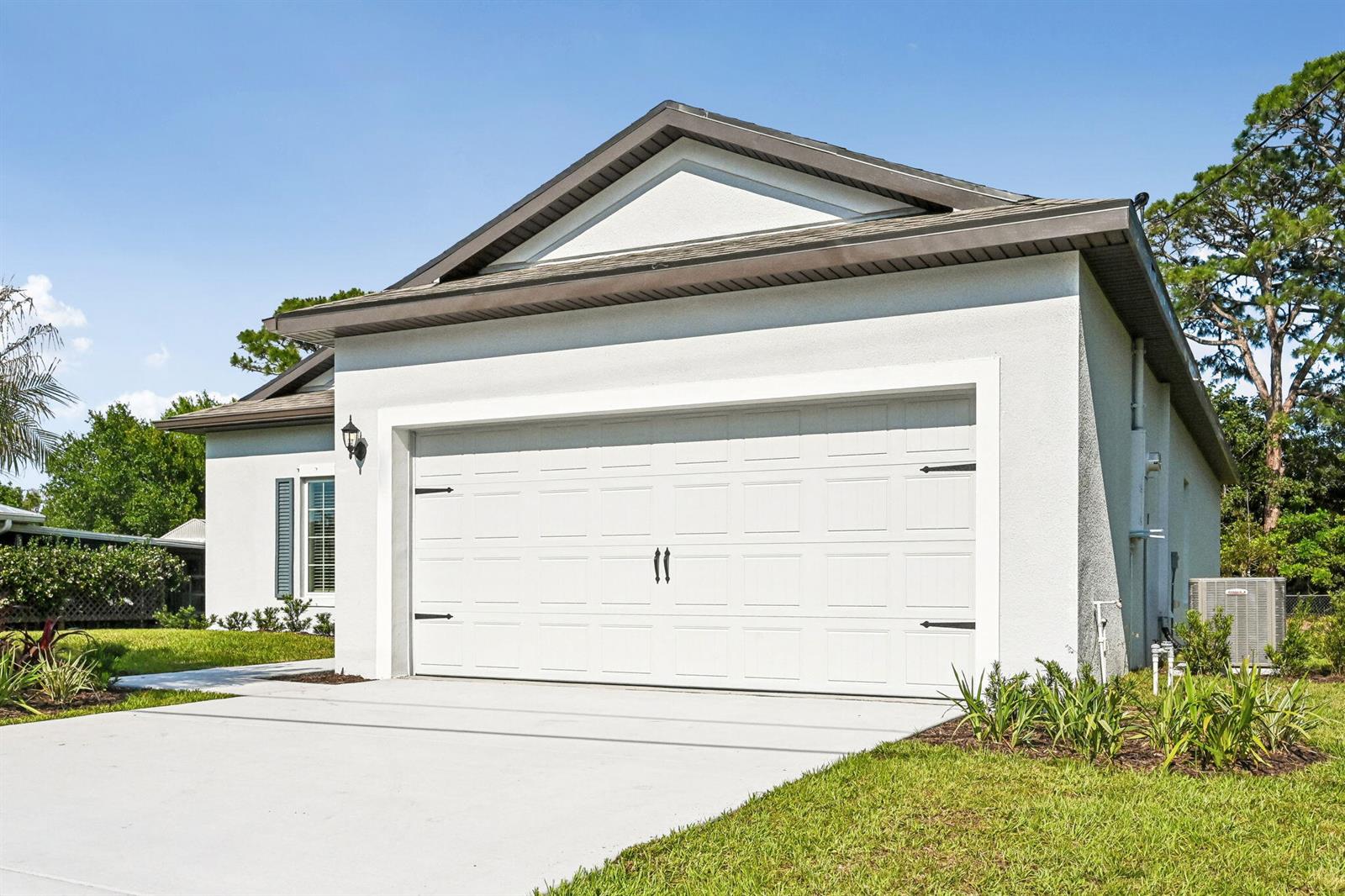 A white house exterior features a two-car garage, a concrete driveway, and a gabled roof — 5019 Sunset Boulevard, Fort Pierce FL 34982, FORT PIERCE, FL