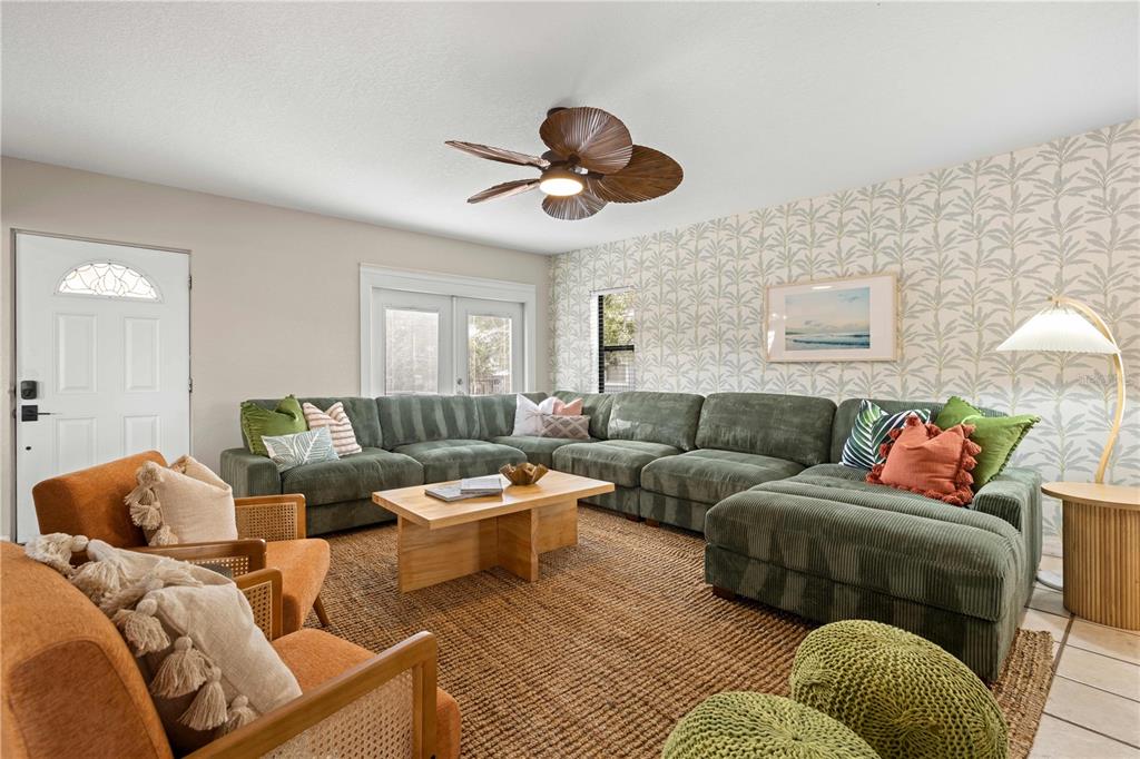 A living room features a large green sectional sofa, orange armchairs, and patterned wallpaper — 2302 BAY BOULEVARD, INDIAN ROCKS BEACH, FL
