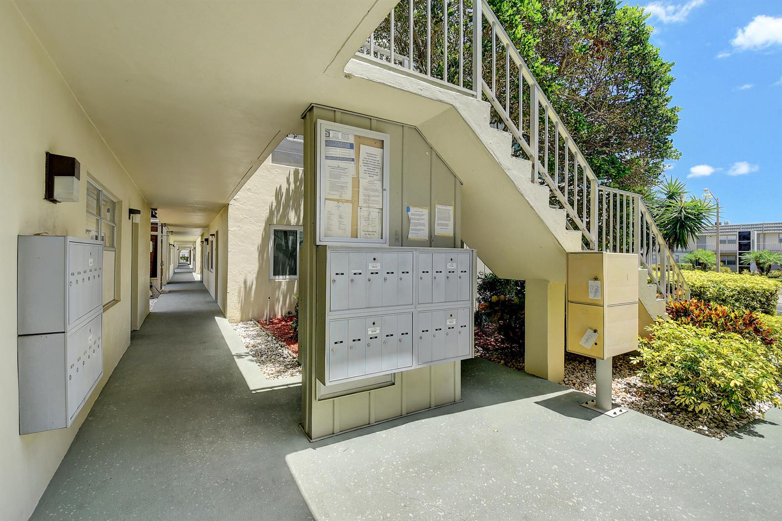 An outdoor apartment complex walkway features a staircase, mailboxes, and a community bulletin board — 318 Monaco Boulevard # G, Delray Beach FL 33446, DELRAY BEACH, FL