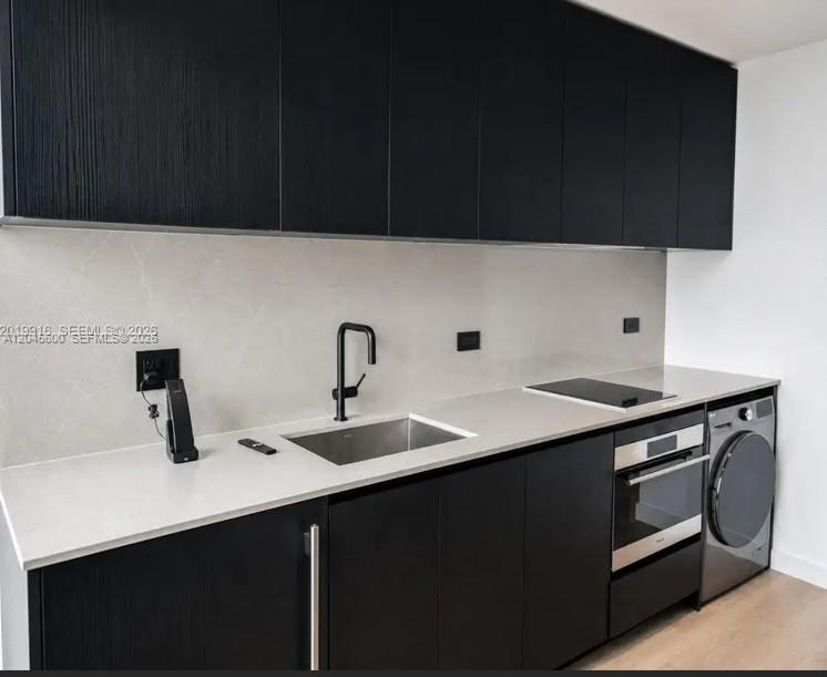A modern kitchen features black cabinets, a light stone countertop, a sink, and a built-in washer — 20 NE 11th ST # 4807A, Miami FL 33132, MIAMI, FL