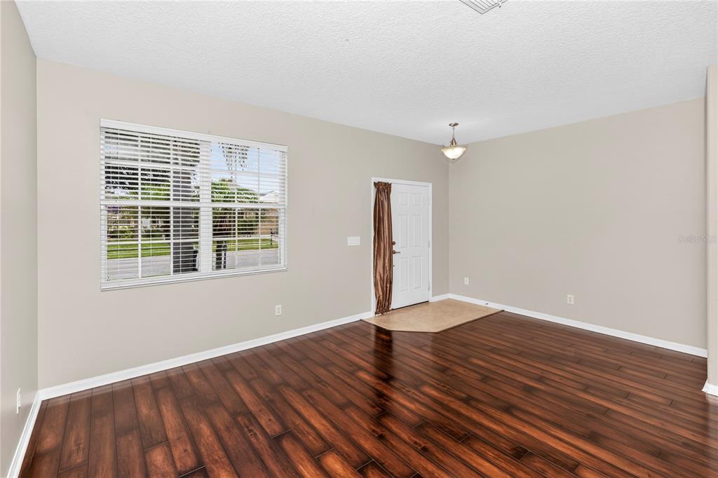 An empty room with dark wood flooring, beige walls, a window with blinds, and an entryway — 14249 QUEENSIDE STREET, ORLANDO, FL