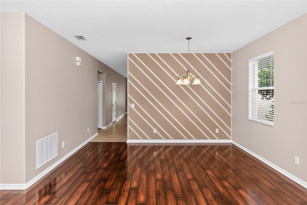 A dining room with dark hardwood floors, a diagonal-striped accent wall, and a hanging chandelier — 14249 QUEENSIDE STREET, ORLANDO, FL