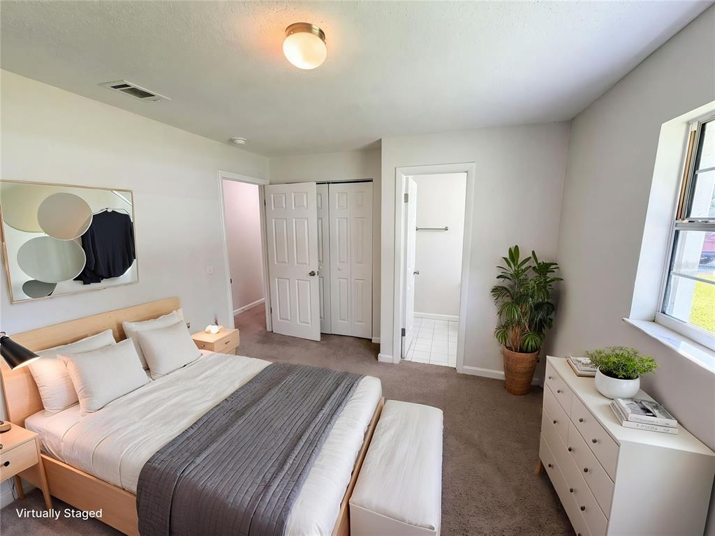 A bedroom with a bed, dresser, closet, and bathroom door, featuring carpeted floors and walls — 1057 LAKEMOOR BOULEVARD, ROCKLEDGE, FL