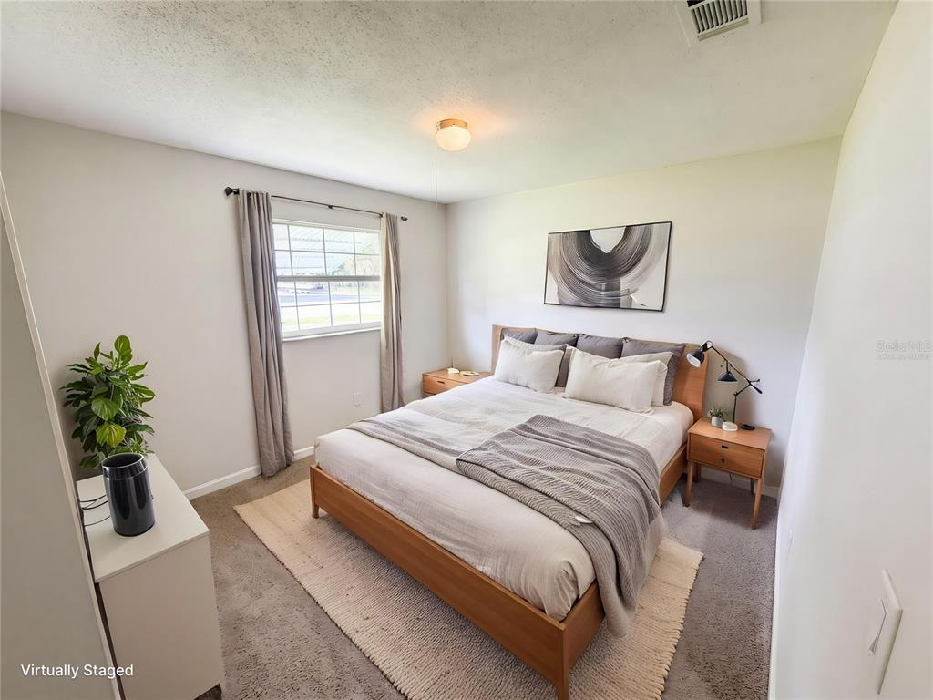 A virtually staged bedroom features a wooden bed frame, gray carpet, and a window — 1057 LAKEMOOR BOULEVARD, ROCKLEDGE, FL