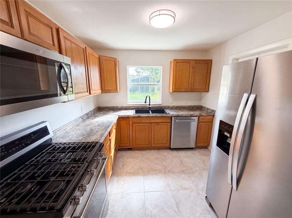 A kitchen features wood cabinets, stainless steel appliances, a double sink, and tile flooring — 1057 LAKEMOOR BOULEVARD, ROCKLEDGE, FL