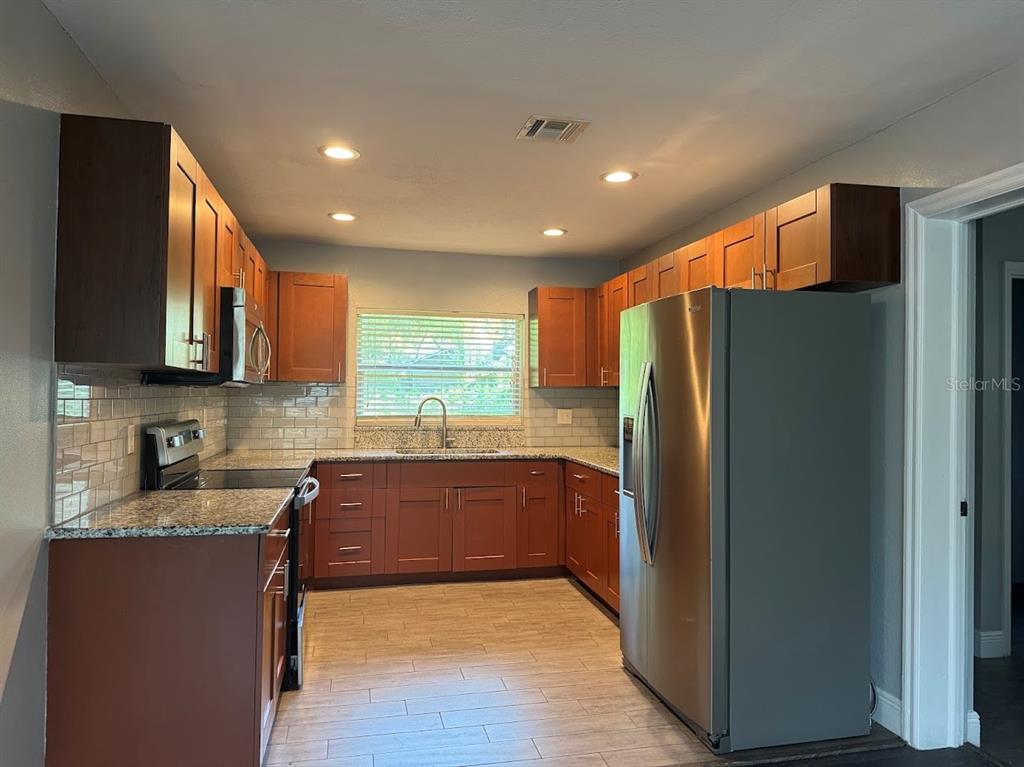 A kitchen features wood cabinets, granite countertops, stainless steel appliances, and light-colored tile flooring — 2125 CARLTON DRIVE, ORLANDO, FL