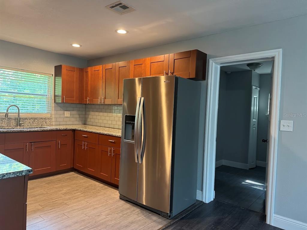 A kitchen features wood cabinets, granite countertops, stainless steel appliances, and light gray walls — 2125 CARLTON DRIVE, ORLANDO, FL