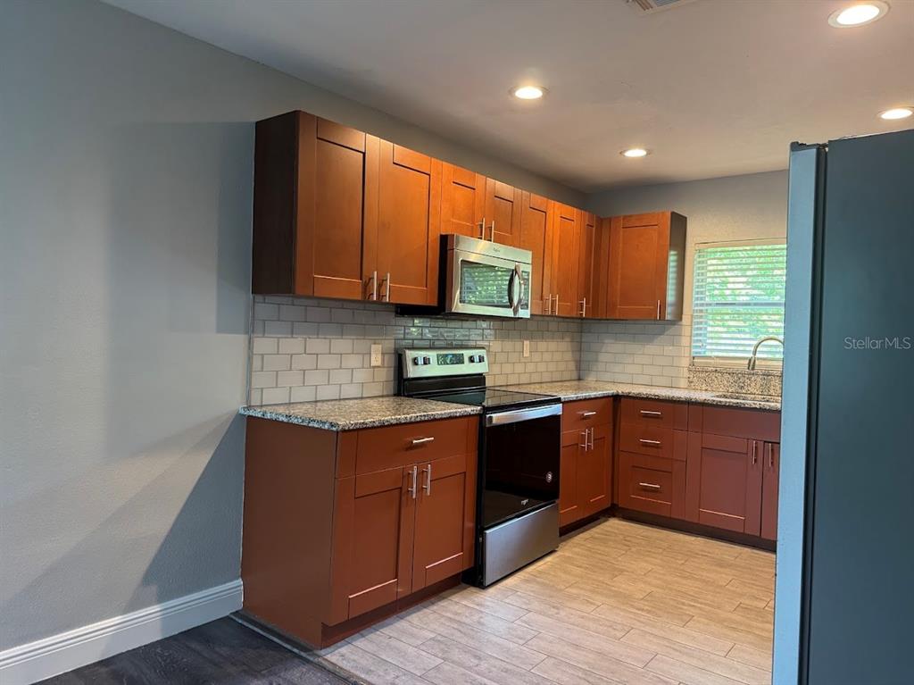A kitchen features wood cabinets, granite countertops, a subway tile backsplash, and stainless steel appliances — 2125 CARLTON DRIVE, ORLANDO, FL