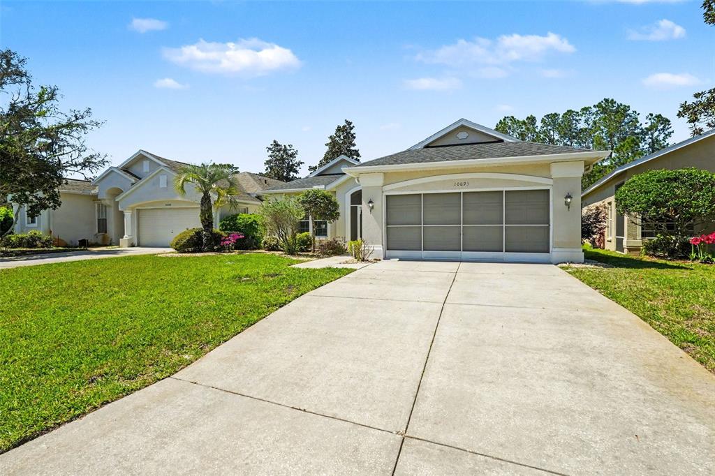 A single-story suburban house with a concrete driveway and a screened garage door — 10093 HOLLY BERRY DRIVE, WEEKI WACHEE, FL