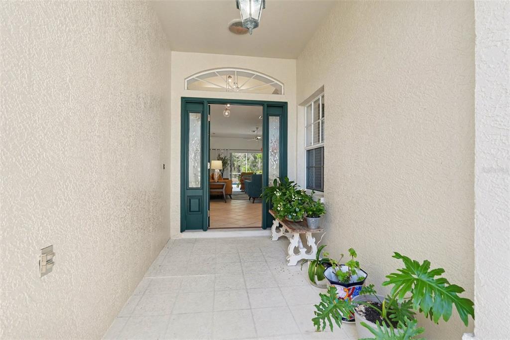 A covered entryway features a teal front door, tiled flooring, and potted plants on a bench — 10093 HOLLY BERRY DRIVE, WEEKI WACHEE, FL