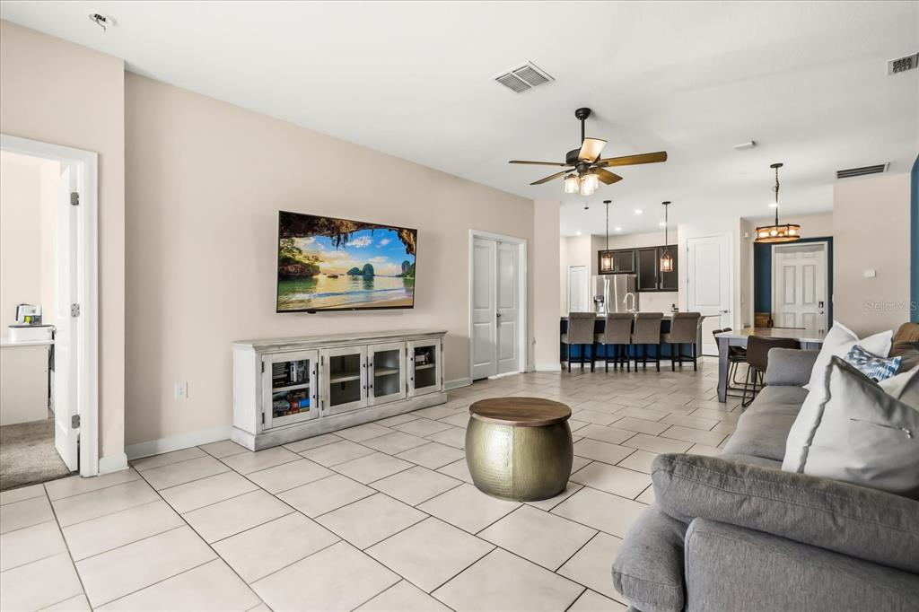 A living room with tile flooring, a wall-mounted television, and an open kitchen area — 133 TAFT DRIVE, DAVENPORT, FL