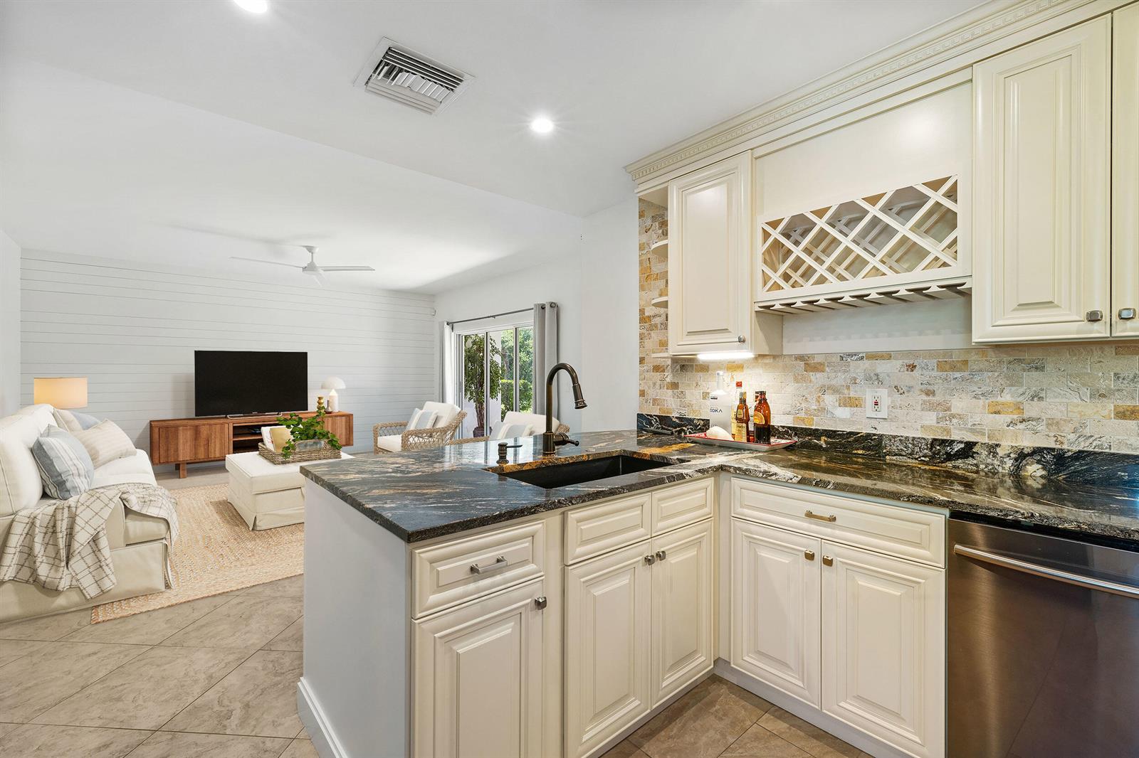 A kitchen with cream cabinets, dark granite countertops, and a stone backsplash overlooks a living room — 2703 N Fairway Dr Drive N, Jupiter FL 33477, JUPITER, FL