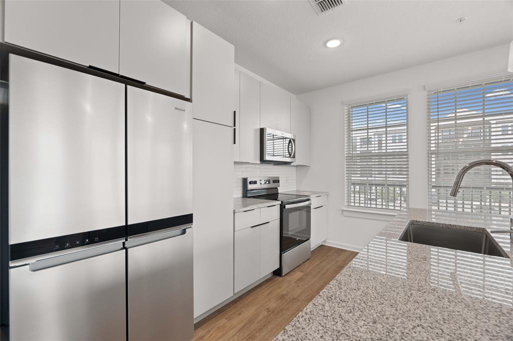 A modern kitchen features white cabinets, stainless steel appliances, granite countertops, and a sink island — 1700 RANCH ROAD UNIT C1-7213, NOKOMIS, FL