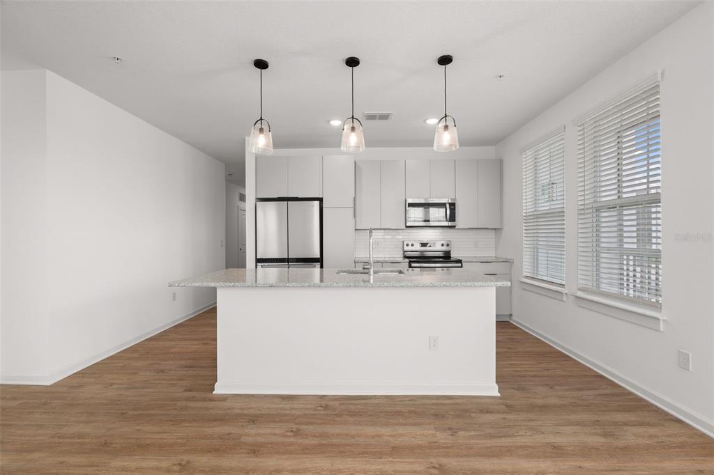 A modern kitchen features a white island, stainless steel appliances, and light wood-look flooring — 1700 RANCH ROAD UNIT C1-7213, NOKOMIS, FL