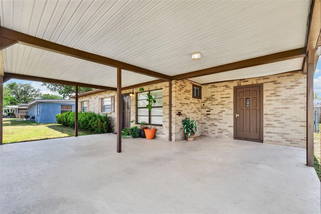 A covered concrete carport attached to a single-story brick house with a brown door — 3004 DREWERY AVENUE, LAKELAND, FL