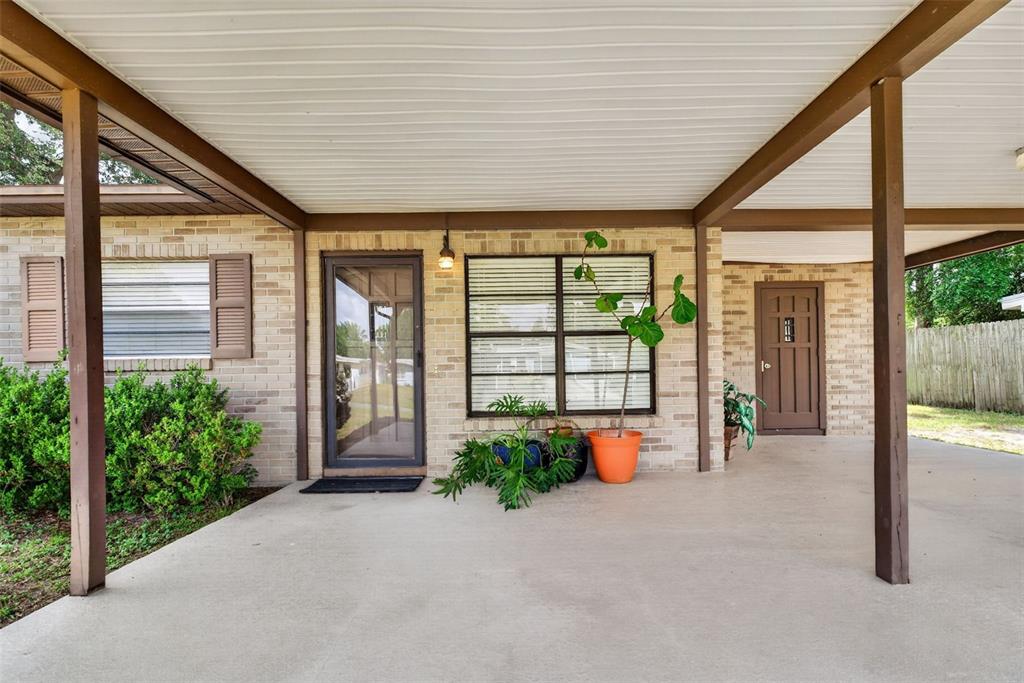A covered concrete patio features a brick exterior, a glass front door, and a side entrance — 3004 DREWERY AVENUE, LAKELAND, FL