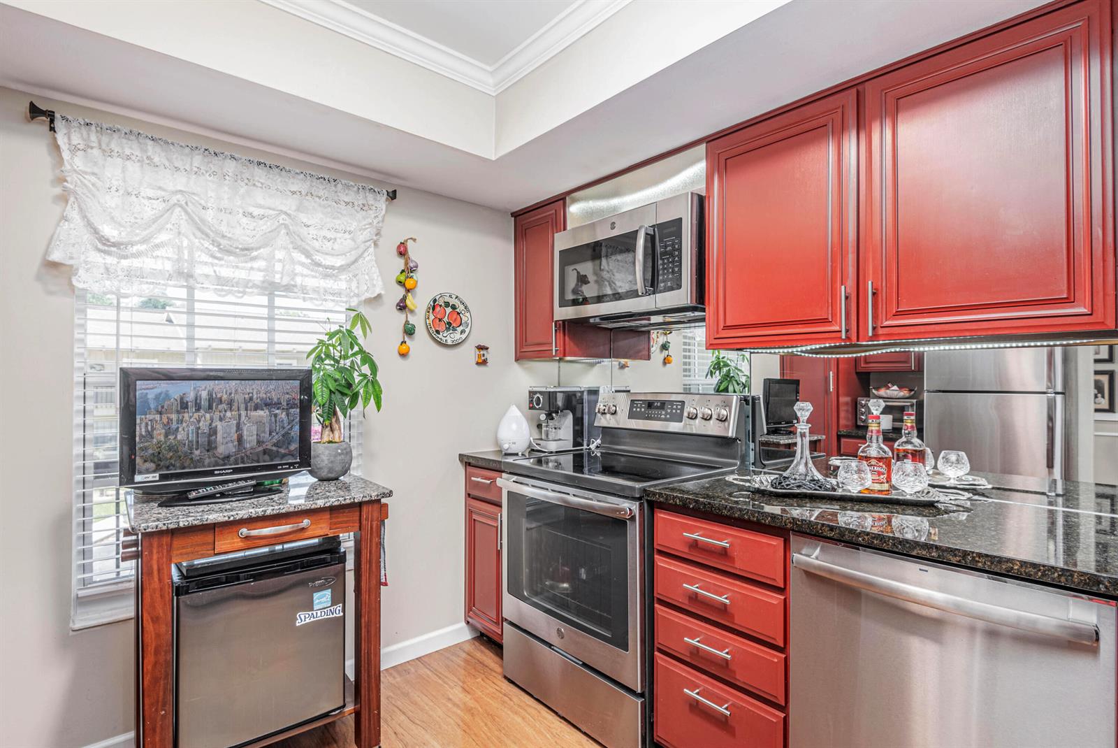 A kitchen features red cabinets, stainless steel appliances, granite countertops, and a small beverage refrigerator — 18560 SE Wood Haven Lane # G, Jupiter FL 33469, JUPITER, FL