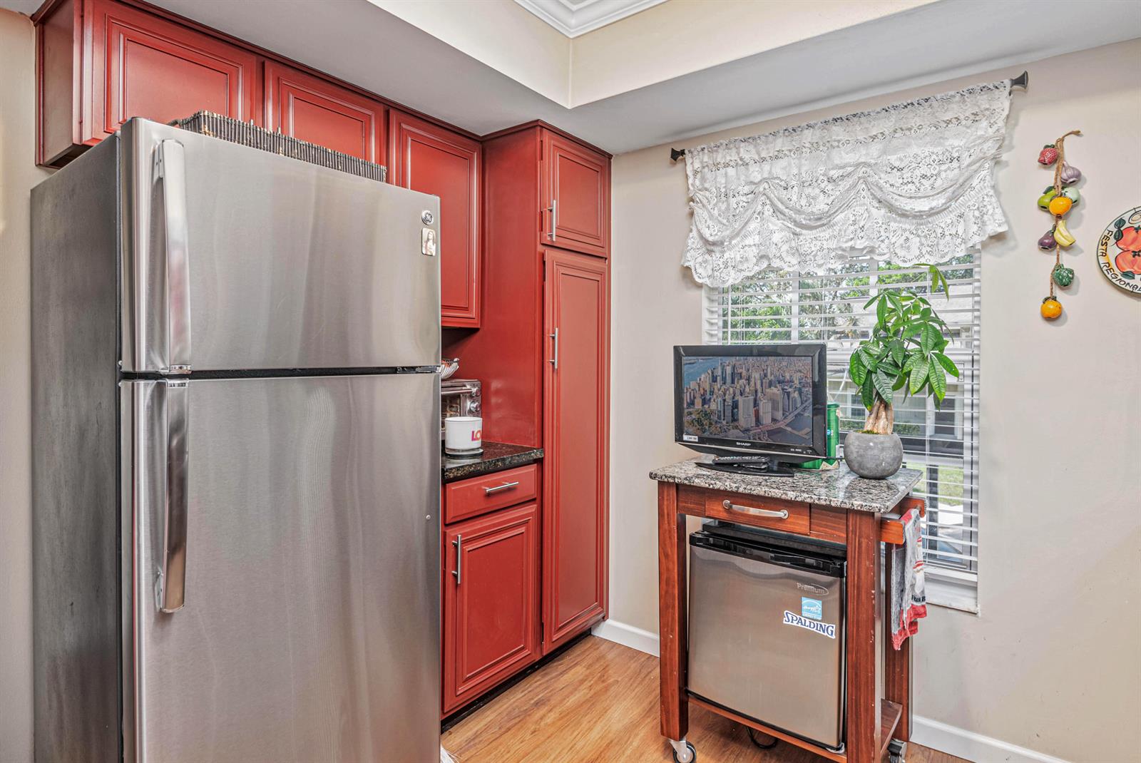 A kitchen features red cabinets, a stainless steel refrigerator, and a small rolling cart — 18560 SE Wood Haven Lane # G, Jupiter FL 33469, JUPITER, FL