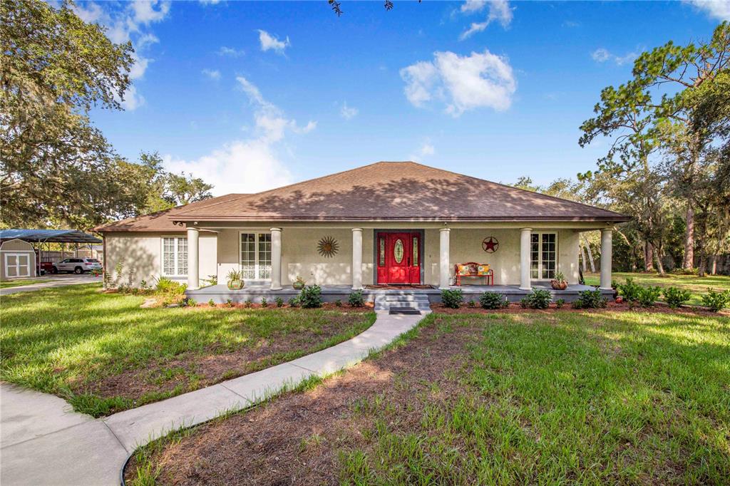 A single-story house with a red front door, covered porch, and columns sits on grass — 10740 JIM EDWARDS ROAD, HAINES CITY, FL
