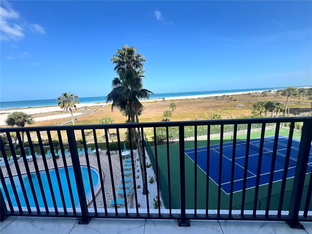 A balcony view overlooking a swimming pool, tennis court, beach, and the ocean — 1250 GULF BOULEVARD UNIT 405, CLEARWATER, FL