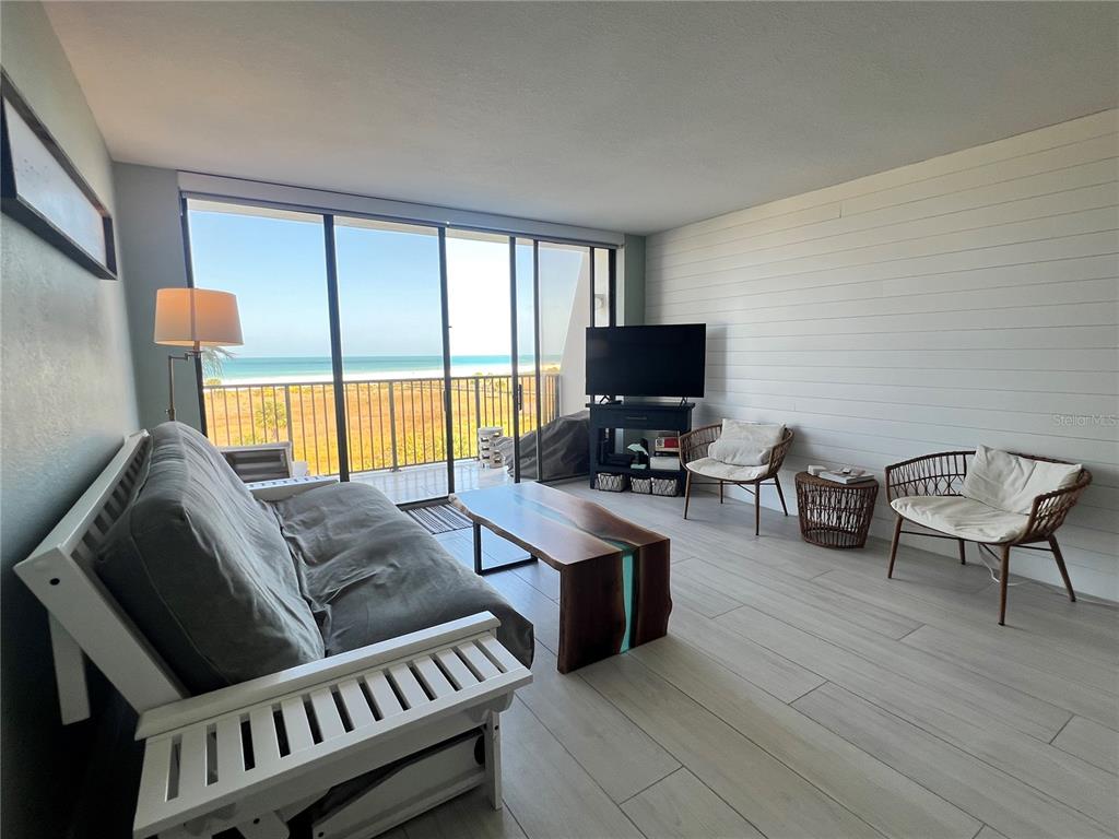 A living room with a futon, wood coffee table, and sliding doors overlooking the beach — 1250 GULF BOULEVARD UNIT 405, CLEARWATER, FL