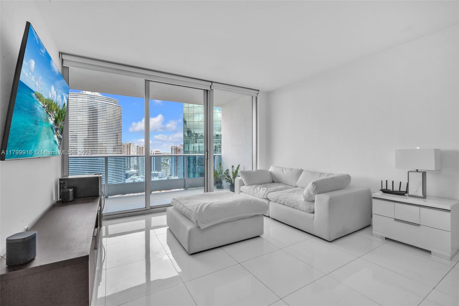 A modern living room features white tile floors, a white sofa, and a balcony view — 200 Biscayne Boulevard Way # 4012, Miami FL 33131, MIAMI, FL