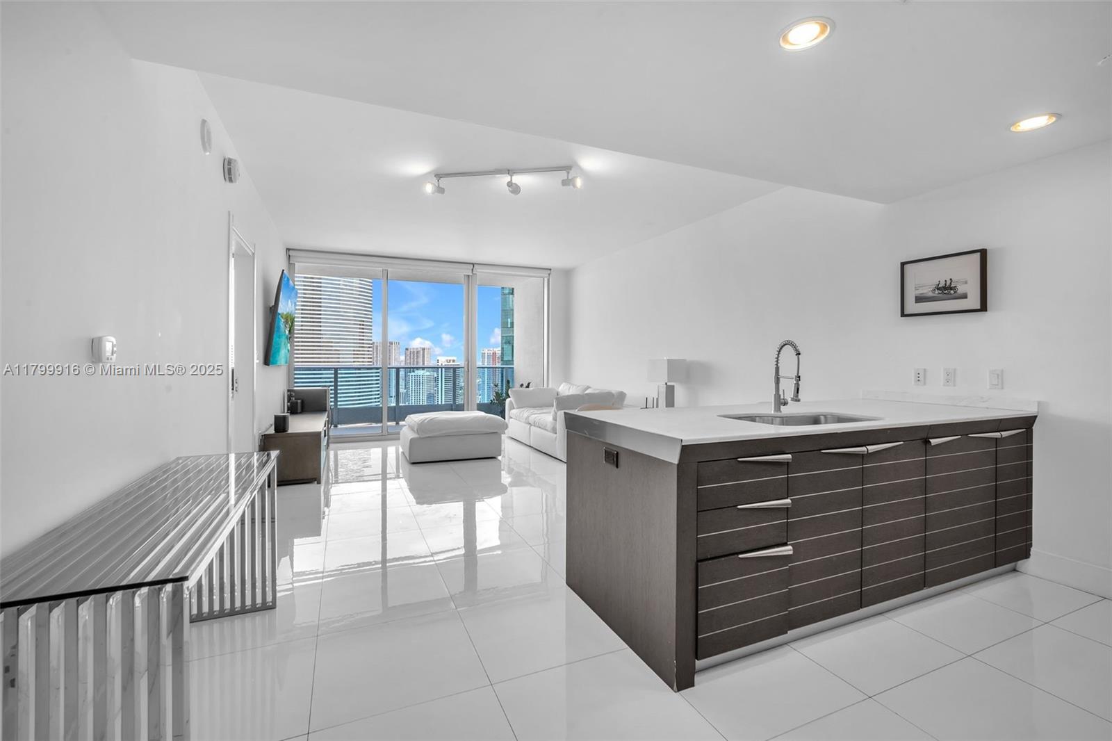 A modern kitchen island with dark cabinetry sits in an open-concept living area with tile floors — 200 Biscayne Boulevard Way # 4012, Miami FL 33131, MIAMI, FL